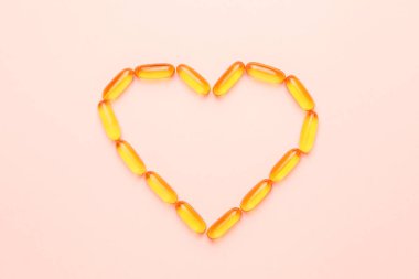 Renk arkaplanındaki balık yağı kapsüllerinden yapılmış kalp şekli