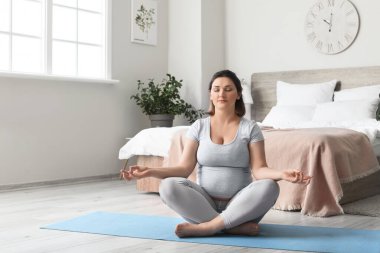 Genç hamile kadın evde yoga yapıyor.
