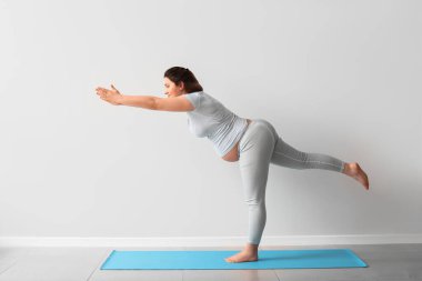 Genç hamile kadın ışık duvarının yanında yoga yapıyor.