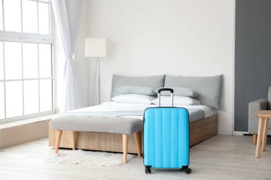 Otel odasında yatağın yanındaki bavul.