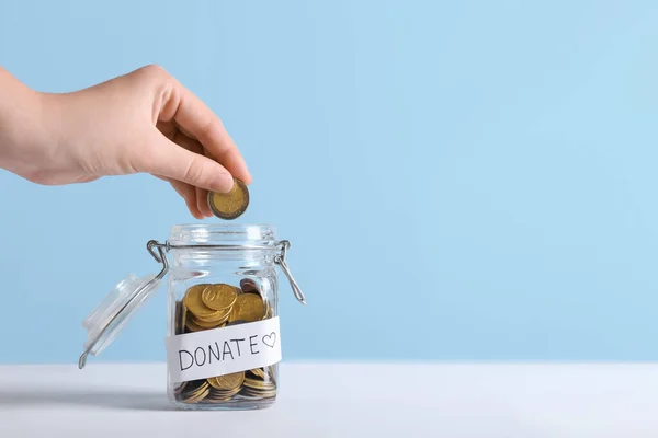 Woman putting coin in jar on table. Concept of donations