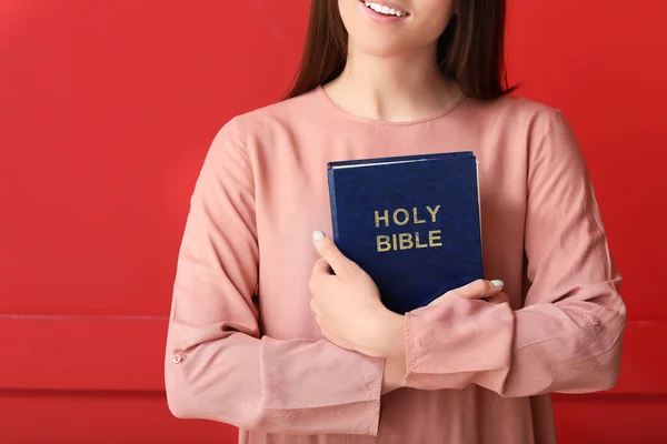 Young woman with Bible on color background