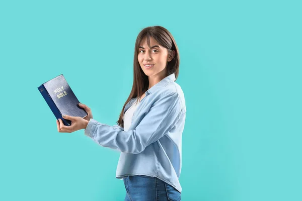 Young woman with Bible on color background