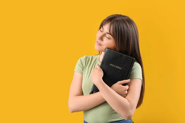 Young woman with Bible on color background