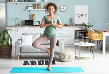 Genç hamile kadın evde yoga yapıyor.