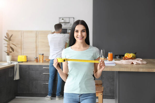 Young woman with measuring tape in kitchen