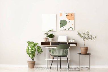 Modern dizüstü bilgisayarlı rahat bir iş yeri ve ışık duvarının yanında bitkiler.