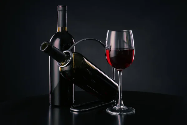 Holder with bottles and glass of wine on dark background