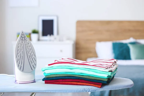 Stack of clean clothes on ironing board in room