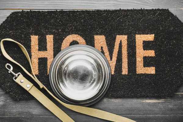 Door mat, pet bowl and leash on wooden background