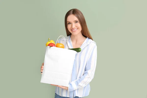 Young woman holding bag with food on color background