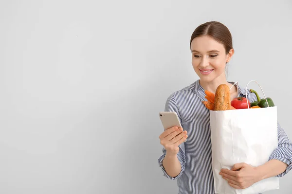 Young woman with food in bag and mobile phone on light background