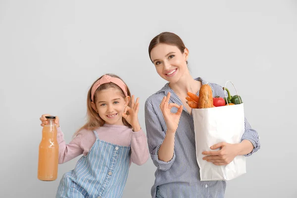Mother and daughter with food in bag showing OK gesture on light background