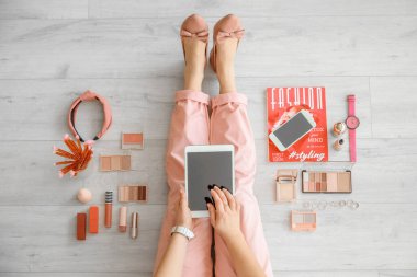 Modern tablet bilgisayarı, cep telefonu ve dekoratif kozmetik ürünleriyle makyaj sanatçısı yerde oturuyor.