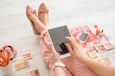 Modern tablet bilgisayarı ve dekoratif kozmetik ürünleriyle makyaj sanatçısı yerde oturuyor.