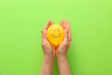 Renkli arka planda çizilmiş gülen yüzlü hava balonu tutan kadın eller.