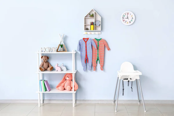Rack with toys and baby clothes hanging on color wall