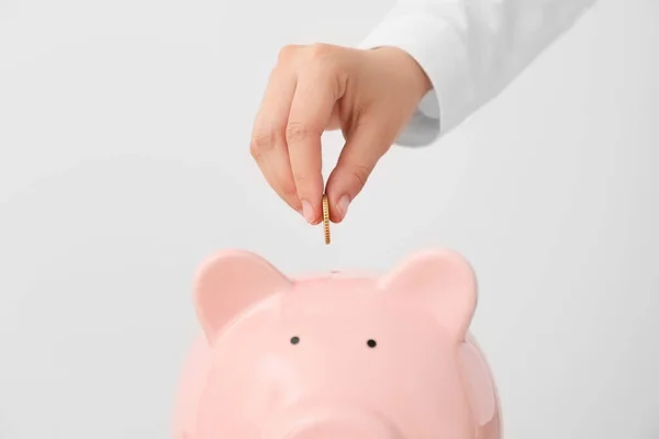 Woman Putting Money Piggy Bank Light Background — Stock Photo, Image