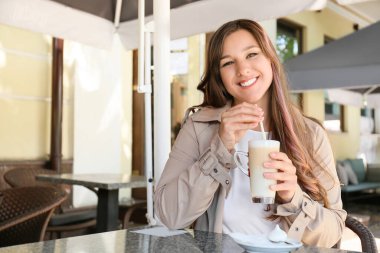Açık kafede sıcak kahve içen genç bir kadın.