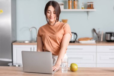 Mutfakta dizüstü bilgisayarı olan güzel bir kadın.