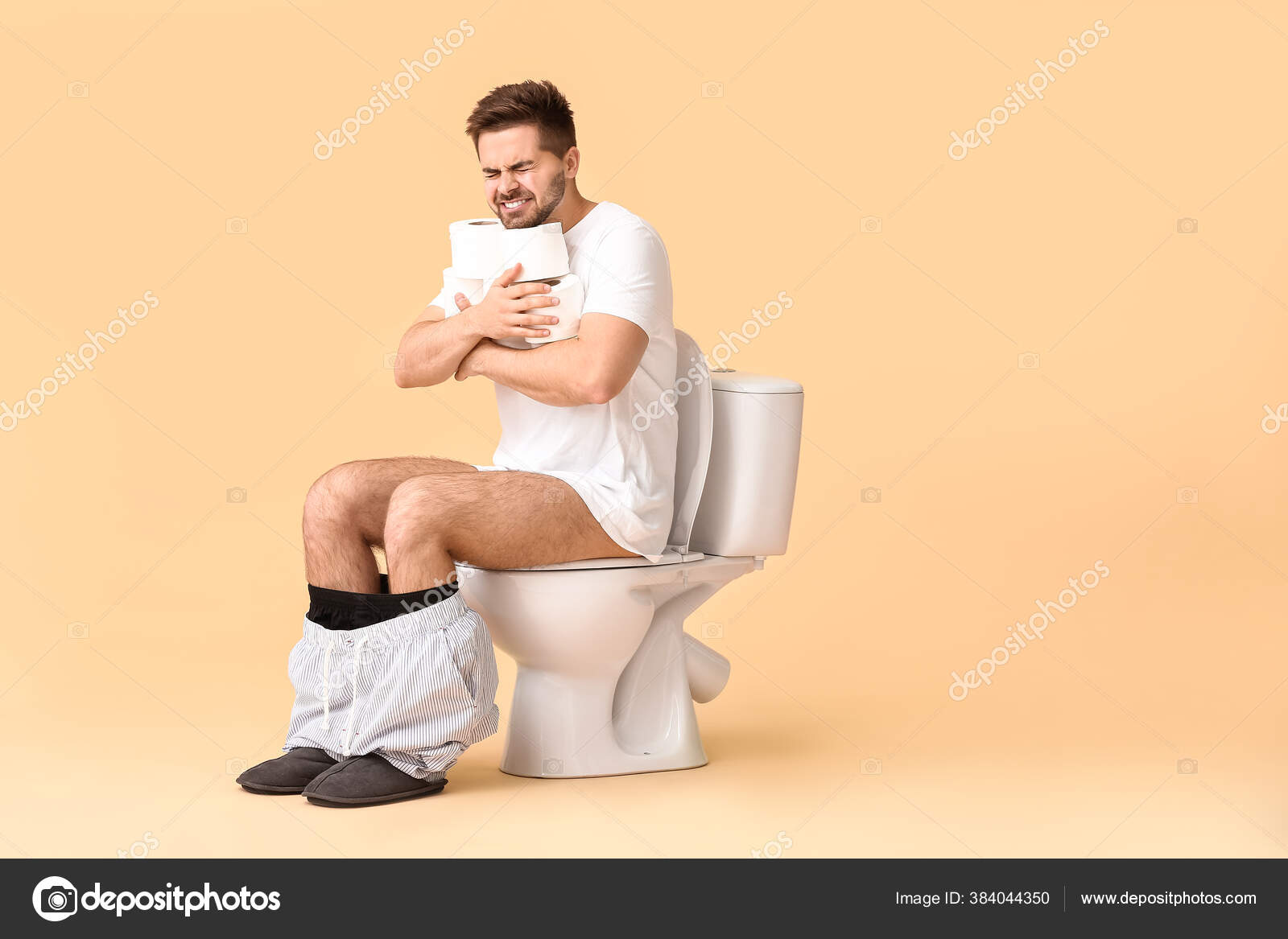 背景色を背景にトイレのボウルに座って紙のロールを持つ若い男 