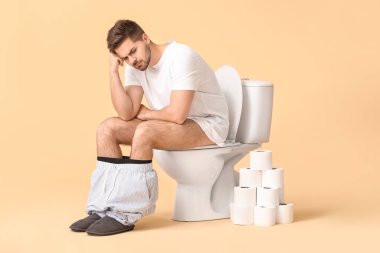 Elinde rulo kağıtla klozetin üzerinde oturan genç bir adam.