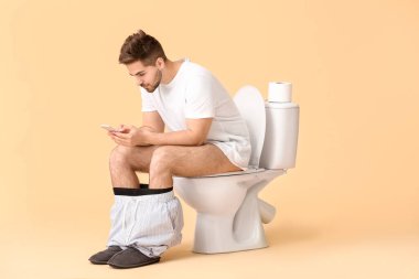Cep telefonlu genç adam klozetin üzerinde oturuyor.