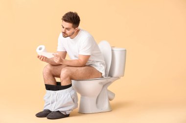 Genç adam klozetin üzerinde oturuyor.