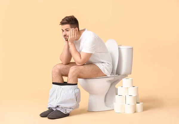 Jovem Com Rolos Papel Sentado Vaso Sanitário Contra Fundo Cor — Fotografia de Stock