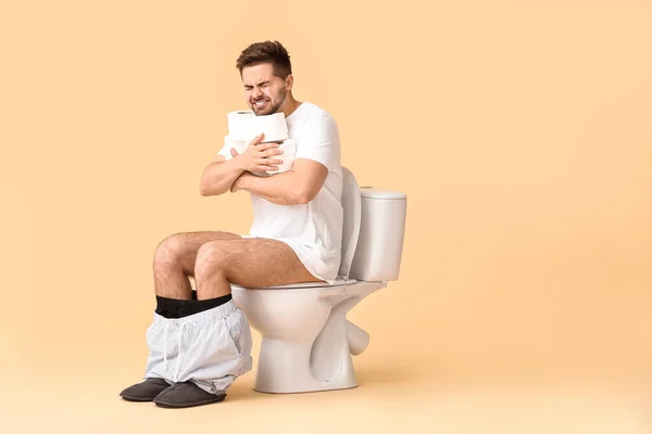 Young Man Rolls Paper Sitting Toilet Bowl Color Background — Stock Photo, Image