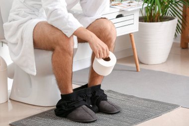 Genç adam tuvalette klozette oturuyor.