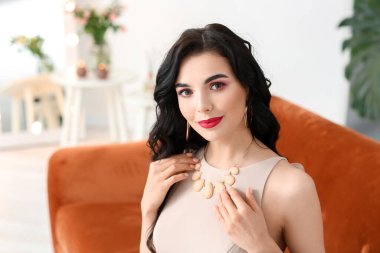 Evin içinde şık takılar takan güzel genç bir kadın.