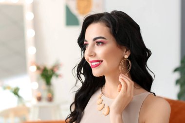 Evin içinde şık takılar takan güzel genç bir kadın.