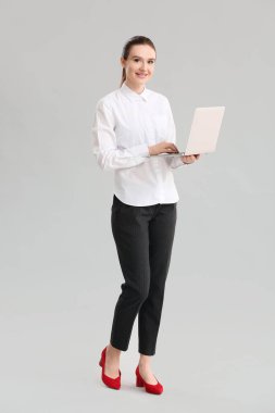 Gri arka planda dizüstü bilgisayarı olan genç bir iş kadını.