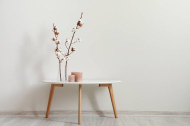 Pamuk çiçekli şık bir masa ve ışık duvarının yanında aroma mumları.