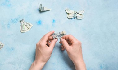 Masadaki banknotlardan origami figürleri yapan kadın.