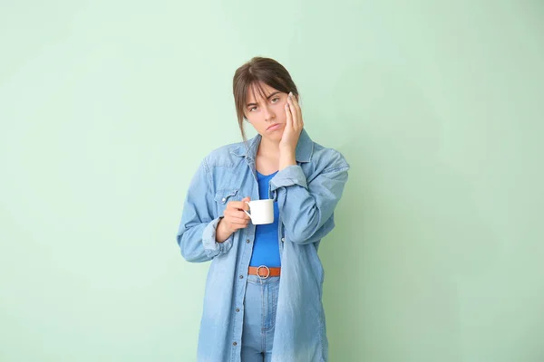 Tired woman with cup of coffee on color background. Concept of sleep deprivation