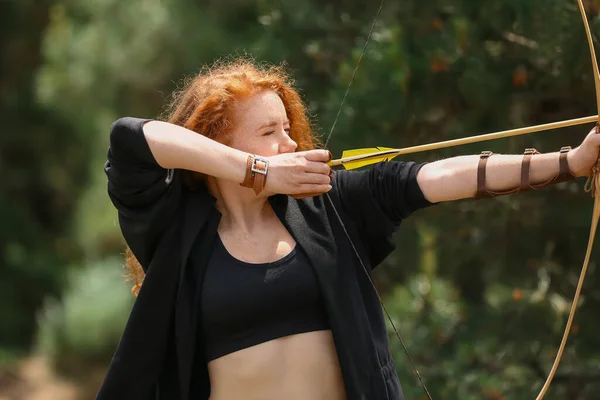 Sporty young woman practicing archery outdoors