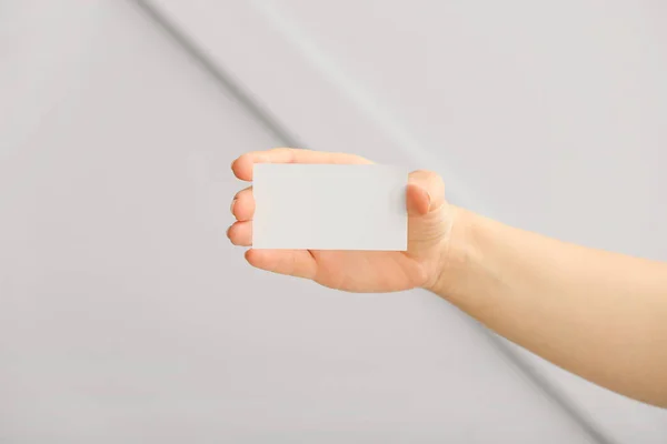 Female hand with blank business card on light background