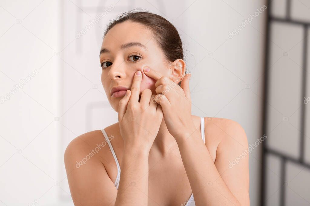 Young woman with acne problem squishing pimples at home