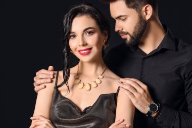 Siyah arka planda şık aksesuarlar giyen genç bir çift.