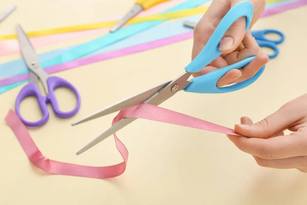 Woman cutting ribbons on color background