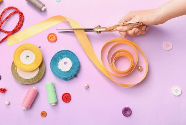 Renk arkaplanındaki makas, kurdele, iplik ve düğmelerle terzi eli