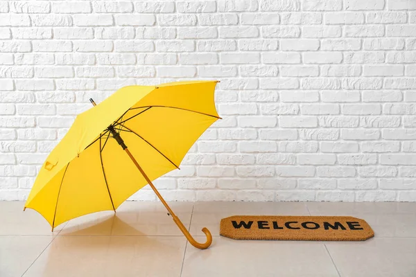 Stylish umbrella and door mat near white brick wall