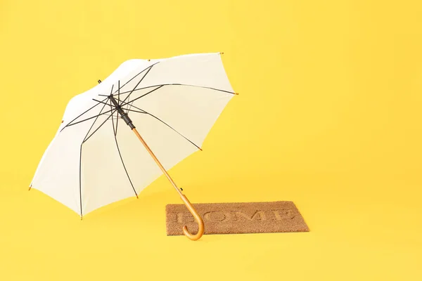 Stylish umbrella and door mat on color background