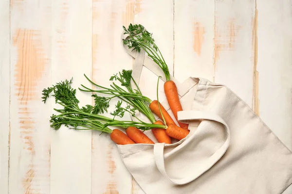 Eco bag with fresh carrots on white wooden background