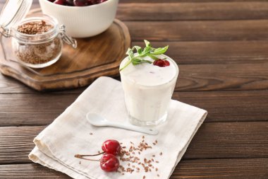 Tahta arka planda kiraz ve keten tohumlu bir bardak yoğurt.