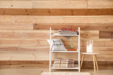 Ahşap duvarın yanında ekose, yastık ve dekorlu raf ünitesi.