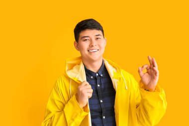 Yağmurluklu genç Asyalı adam, arka planda iyi görünüyor.