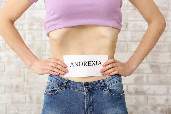 Woman with word ANOREXIA on paper sheet, closeup. Concept of anorexia